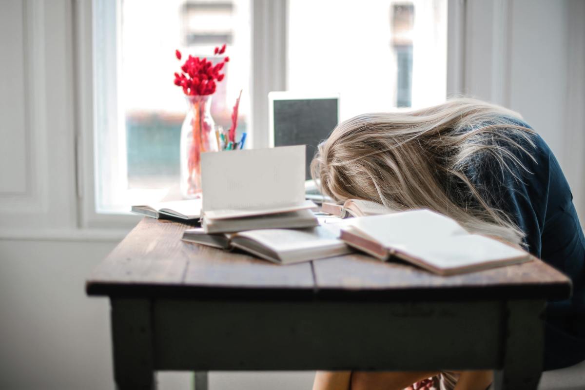 Tired woman rests her head on a pile of books