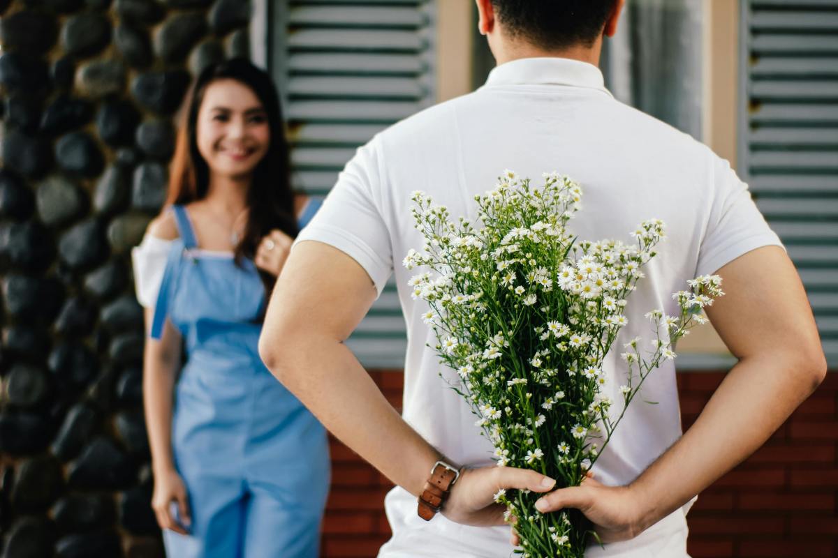 Man holding a bouquet behind his back while a woman is standing in front of him