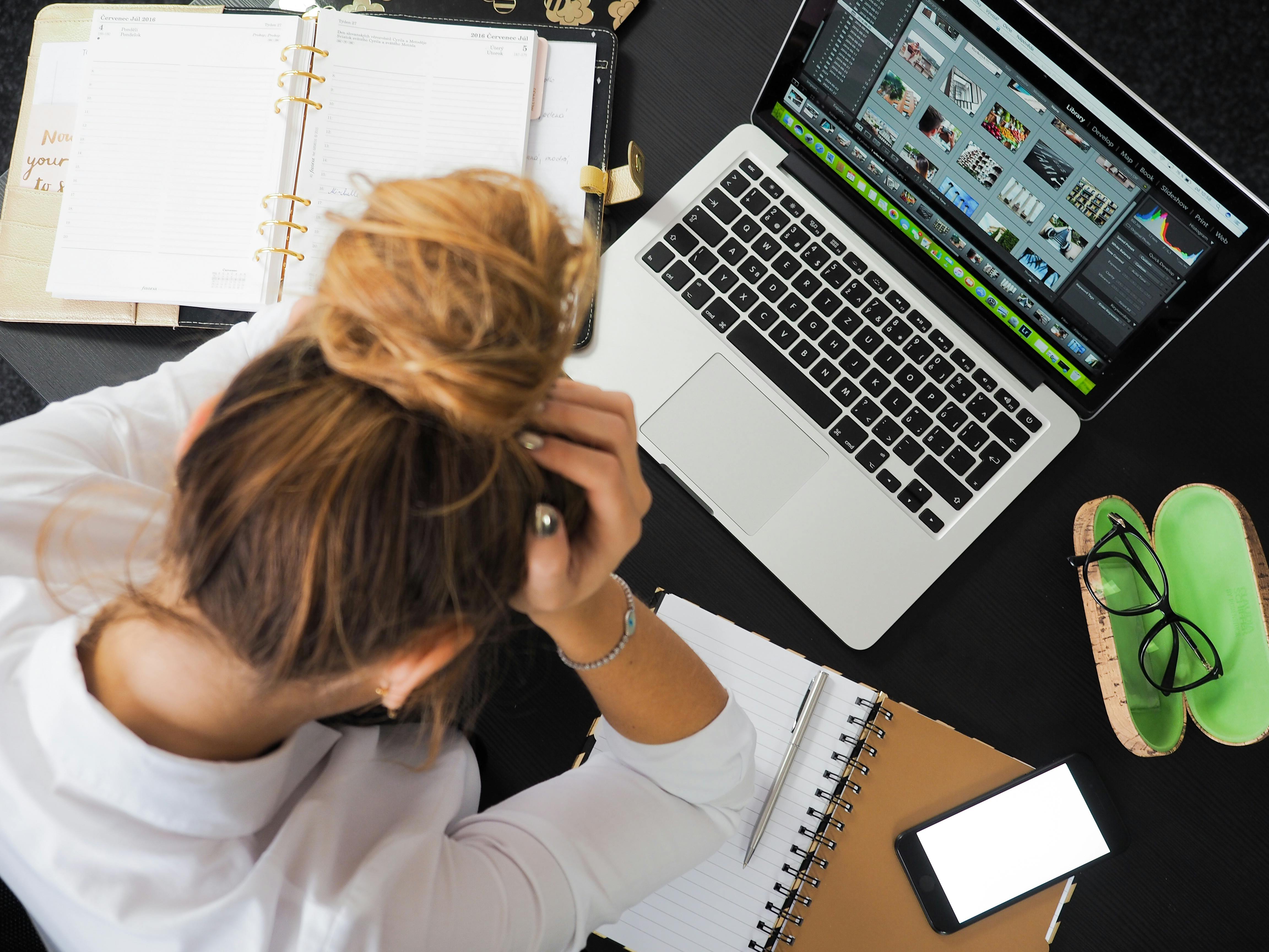 A woman sits at her desk in front of a laptop with her head in her hands
